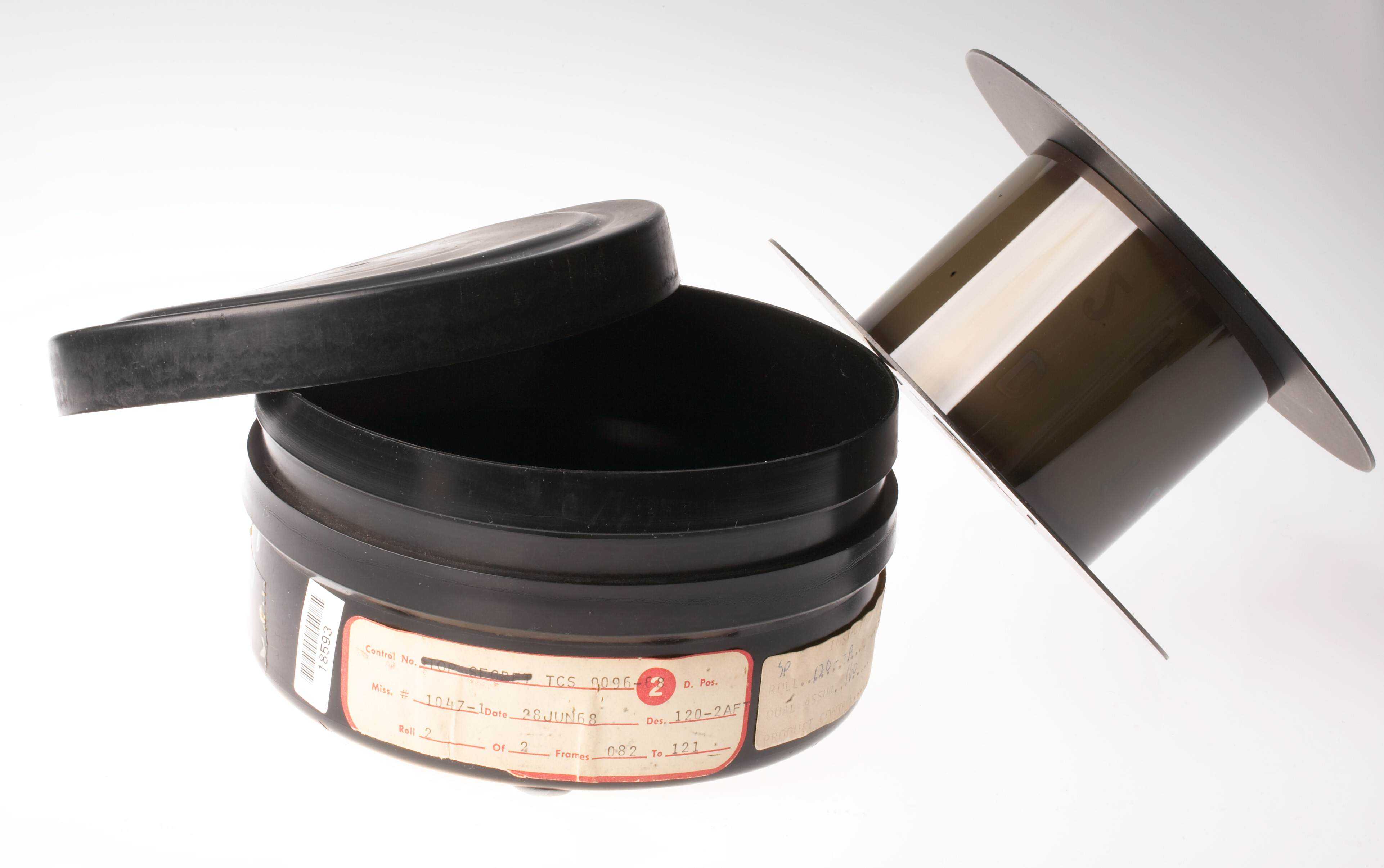 A film canister with several labels next to an empty film reel.