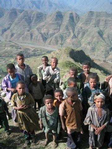 A color photograph taken by Gregg of a group of children standing atop a cliff with a lush green valley in the background.