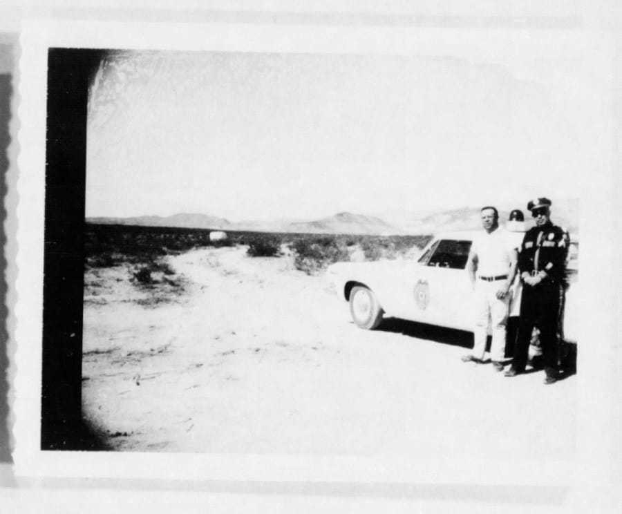 A blurry black and white photograph of a police officer and man standing outside a car.
