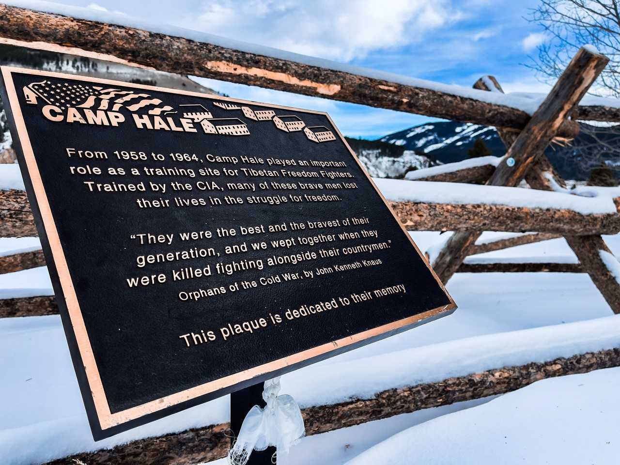 black and gold roadside plaque with a wooden fence behind it and snow covering the fence and ground