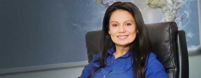 A photograph of a CIA employee wearing a blue top, sitting in a black leather chair in front of a world map.