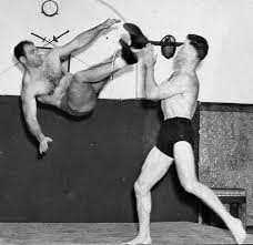 black and white photo of two wrestlers, one jumping into the air with their foot flying toward the others face.