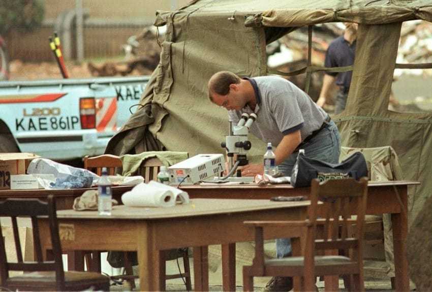 A man, bending over a table with a microscope, in the field.