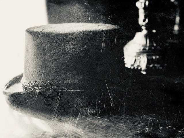 A black and white faded image of a black top hat sitting on a table.