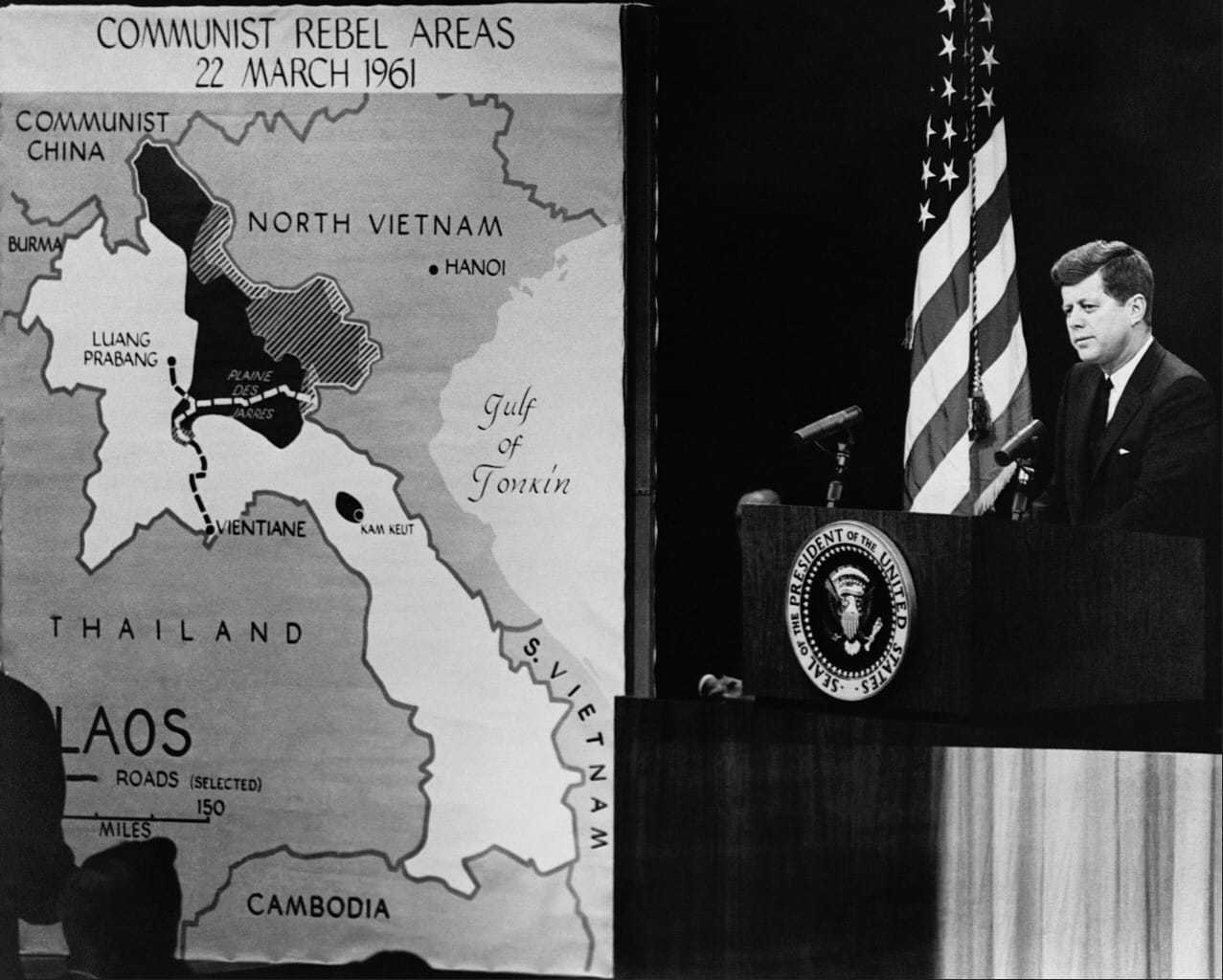 President Kennedy speaking behind the podium with a map of Vietnam on display to his right.