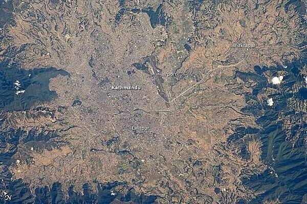 The capital and largest city of Nepal, Kathmandu, occupies much of the valley located near the center of the country. Nepal is home to much of the Himalaya mountain range between Tibet (China) to the north and India to the south. Geological and fossil evidence indicates that the Kathmandu Valley was covered by a large lake between approximately 2.8 million and 10,000 years ago. Paleo-Kathmandu Lake is thought to have drained in phases due to the drying of the regional climate; continuing mountain building-tectonic uplift and faulting-in the region; and the formation of an integrated drainage system, as river channels cut through previous rock ridge dams.
The green, vegetated slopes that ring the Kathmandu metro area (light gray, image center) include both forest reserves and national parks. The metropolitan area is relatively flat compared to the surrounding mountains. Tribhuvan International Airport, near the eastern margin of the city, is the only international airport in Nepal.
Archeological evidence suggests that the human development of Kathmandu, together with the nearby "sister cities" of Lalitpur and Bhaktapur, began almost 2,000 years ago. Today, the three cities form the governmental, cultural, and-as a main access point to the Himalayas for tourism-economic center of the country. Photo courtesy of NASA.