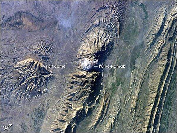 The Zagros Mountains in southwestern Iran present an impressive landscape of long linear ridges and valleys. Formed by collision of the Eurasian and Arabian tectonic plates, the ridges and valleys extend hundreds of kilometers. This astronaut photograph of the southwestern edge of the Zagros mountain belt includes another common feature of the region - a salt dome (Kuh-e-Namak or "mountain of salt" in Farsi). Thick layers of minerals such as halite (table salt) typically accumulate in closed basins during alternating wet and dry climatic conditions. Over geologic time, these layers of salt are buried under younger layers of rock. The pressure from overlying rock layers causes the lower-density salt to flow upwards, bending the overlying rock layers and creating a dome-like structure. Erosion has spectacularly revealed the uplifted tan and brown rock layers surrounding the white Kuh-e-Namak to the northwest and southeast (center of image). Radial drainage patterns indicate another salt dome is located to the southwest (image left center). If the rising plug of salt (called a salt diapir) breaches the surface, it can become a flowing salt glacier. Salt domes are an important target for oil exploration, as the impermeable salt frequently traps petroleum beneath other rock layers. Image courtesy of NASA.