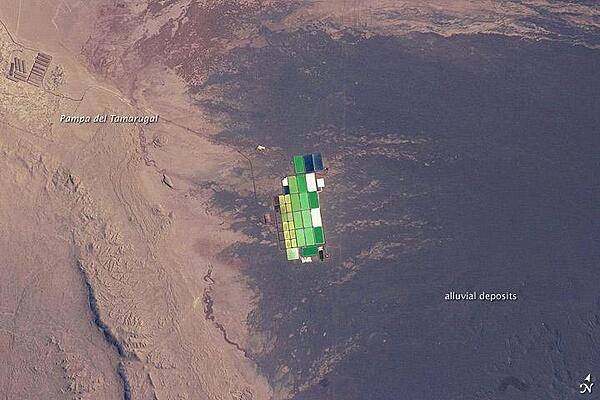 Brightly colored solar evaporation (salt) ponds in a desert landscape give this astronaut photo an unreal quality. The ponds sit near the foot of a long alluvial fan in the Pampa del Tamarugal, the great hyper-arid inner valley of Chile's Atacama Desert. The alluvial fan sediments are dark brown, and they contrast sharply with tan sediments of the Pampa del Tamarugal.
Nitrates and many other minerals are mined in this region. A few extraction pits and ore dumps are visible at upper left. Iodine is one of the products from mining; it is first extracted by heap leaching. Waste liquids from the iodine plants are dried in the tan and brightly colored evaporation ponds to crystallize nitrate salts for collection. The recovered nitrates are mainly used for fertilizer for higher-value crops. They are also used in the manufacture of pharmaceuticals, explosives, glass, and ceramics, as well as in water treatment and metallurgical processes. Image courtesy of NASA.