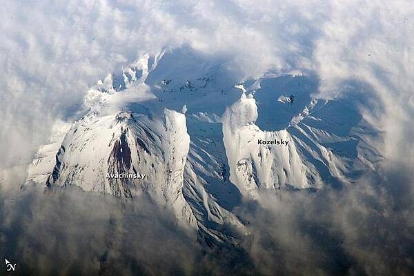 Russia's eastern Kamchatka Peninsula, which extends far into the Pacific Ocean, includes more than 150 volcanoes. While most are not actively erupting, many are considered dangerous due to their eruptive history and proximity to population centers and air travel corridors. This astronaut photo highlights the summit crater and snow-covered slopes of Avachinshy stratovolcano (2,741 m; 8,993 ft) as it pokes above a surrounding cloud deck. The volcano has an extensive historic and geological record of eruptions, the latest activity ocurring in 2008. To the southeast (image right), the large breached crater of Kozelsky volcano also appears above the clouds. Kozelsky is a parasitic cone, formed by the eruption of material from vents along the flank of Avachinsky. Photo courtesy of NASA.