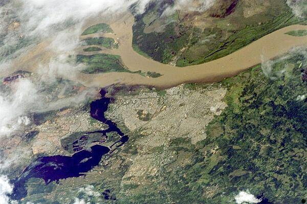 Ciudad Guayana lies on the south bank of the Orinoco River, the second largest in South America, at its confluence with the Caroní River (lower left). Islands have developed in the Orinoco in a wide spot opposite the city (upper left). Guayana is one of the newest cities in Venezuela, constructed in 1961 as a new economic center for the interior of Venezuela, especially for major industries such as iron, steel, and aluminum. The city stretches 40 km (24 mi) along the south bank of the Orinoco and is one of Venezuela's largest. A low barrage (lower left) dams the Caroní as a water supply for the city. The Orinoco River is muddy brown, carrying sediment produced by erosion of the Andes Mountains far to the southwest. By contrast, the Caroní is clear blue, as it drains the ancient landscapes of the Guyana Highlands, where erosion is much slower. A mixing zone can be seen in the middle of this image. The clear Caroní water produces a less muddy zone for tens of kilometers downstream of the confluence (this part of the Orinoco flows almost due east, left to right). Image courtesy of NASA.