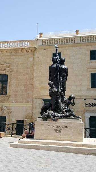 Located in Palace Square, Valletta, the Sette Giugno (Italian for "Seventh of June") Monument commemorates the 1919 uprising against profiteering merchants and the colonial government. This event was a first step towards Maltese independence which arrived in 1964. Sculpted by Anton Agius and inaugurated on 7 June 1986, the monument features six men, two of whom stand defiantly holding the Maltese flag while the other four, representing the victims and the many who were injured in the riots, react to the events - with one succumbing to his wounds. Sette Giugno was made a national holiday in 1989.