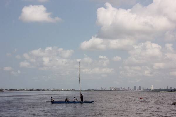 Fishermen ply their trade; the Abidjan skyline appears in the background.
Abidjan is the economic capital of the Ivory Coast. The city expanded quickly after the construction of a new wharf in 1931, followed by its designation as the capital city of the then-French colony in 1933. Abidjan remained the capital of the Ivory Coast after its independence from France in 1960. The completion of the Vridi Canal in 1951 enabled Abidjan to become an important sea port. In 1983, the city of Yamoussoukro was designated as the official political capital of Ivory Coast. However, most political institutions and foreign embassies continue to be located in Abidjan.