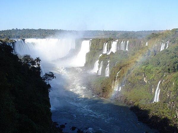 The majestic Iguaçu Falls (Iguazú Falls) on the Brazil-Argentine border. The falls are part of a nearly virgin jungle ecosystem surrounded by national parks on both sides of the cascades. The Iguazú River begins in Parana state of Brazil, then crosses a 1,200-km (750 mi) plateau before reaching a series of faults forming the falls. The falls are shared between Iguazú National Park (Argentina) and Iguaçu National Park (Brazil). The two parks were designated UNESCO World Heritage Sites in 1984 and 1986, respectively. The entire waterfall system consists of some 275 falls that flow over several basaltic layers over an 80 m (262 ft) height and along 2.7 km (1.7 mi) of the Iguazu River.