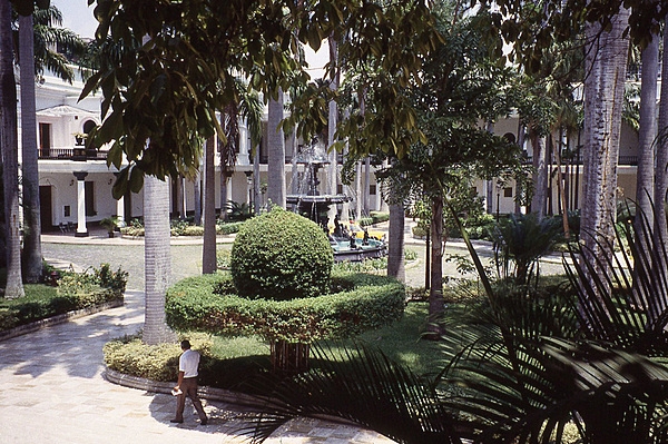 The courtyard of the Federal Legislative Palace in Caracas, Venezuela, with large trees, shrubs, and a fountain.