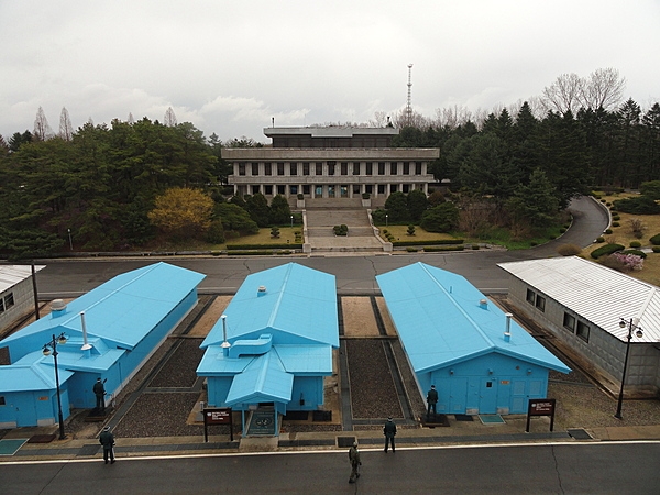 South Korean soldiers standing guard at the Joint Security Area (JSA) between blue UN buildings. The white buildings are North Korean. This view is from the House of Freedom in South Korea looking towards the three-story Panmungak Hall in North Korea.