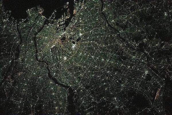 A nighttime view of Tokyo from the International Space Station as it orbited 420 km (261 mi) above the island nation in February 2021. The heart of the city is brightest, with ribbons of lights radiating outward from the center along streets and railways. The regularly spaced bright spots along the ribbons heading out of the downtown area are train stations along public transit routes. The lights of Tokyo are a cooler blue-green color than in many other world cities. The color results from the more widespread use of mercury vapor lighting as opposed to sodium vapor lighting, which produces an orange-yellow light. Photo courtesy of NASA.